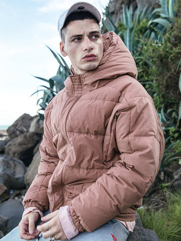 Fashionable young man in pink parka sitting outside looking away